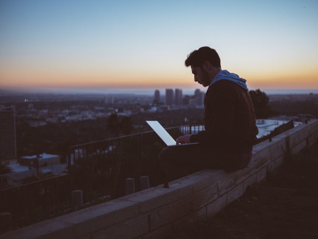 Man sitting on edge of building reading on laptop