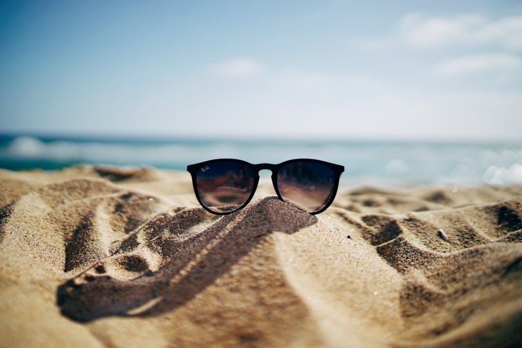 vacation personalization - sunglasses in sand with sea in background and blue sky