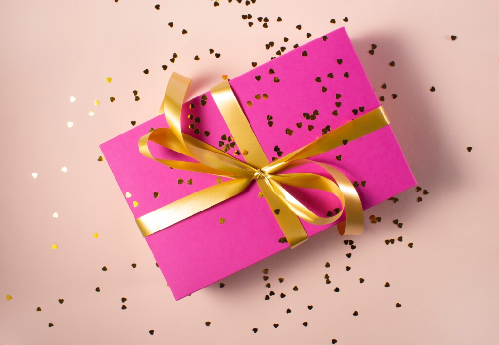pink box wrapped with gold ribbon with sequins