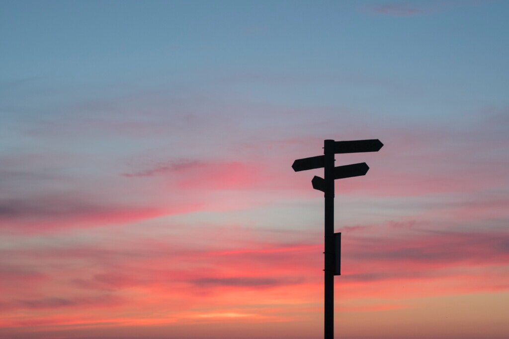 silhouette of sign post on blue sky, fading to pink