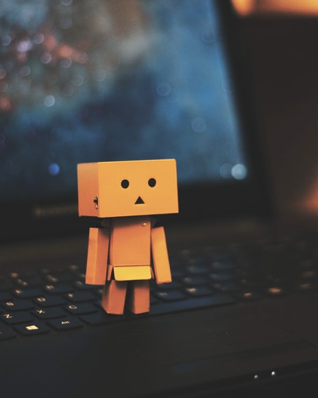 emotions displayed: sadness, indifference. little yellow robot with sad face standing on a laptop keyboard
