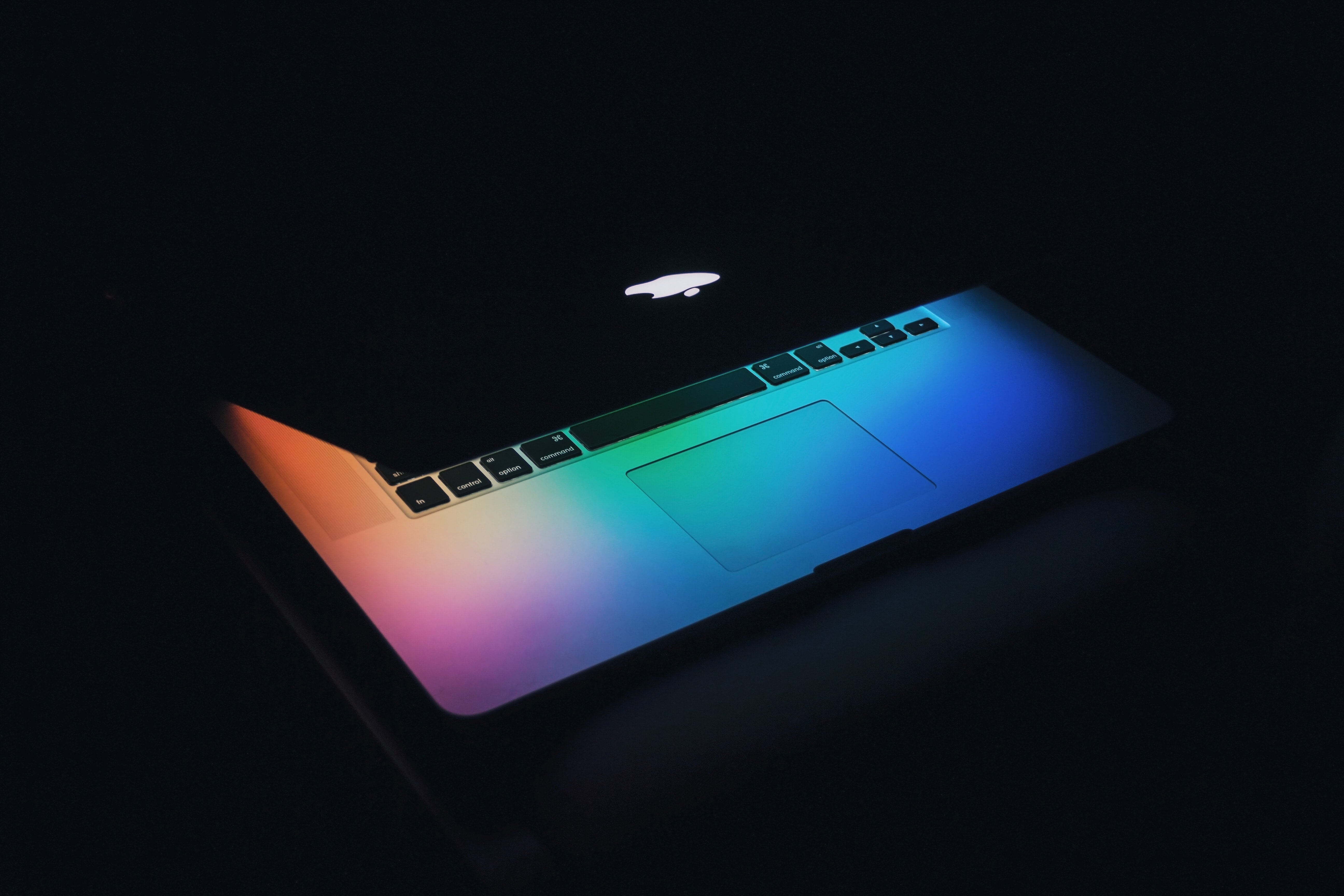Macbook laptop in the dark projecting rainbow colours from screen